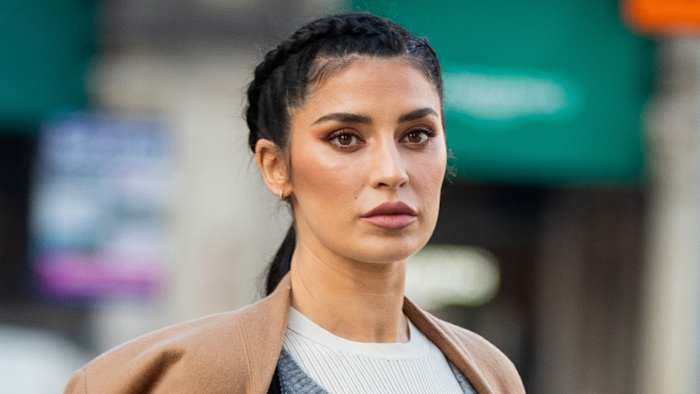 Nicole Williams English poses in a white shirt and tan coat and looks into the distance.